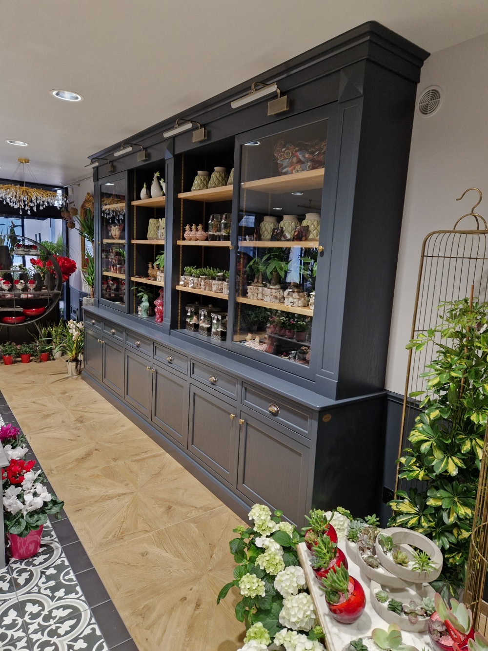 Agencement sur mesure d’un magasin de fleurs avec grande bibliothèque du sol au plafond, plantes et objets de décoration. 